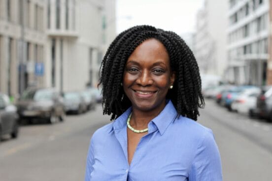 Florence Brokowski-Shekete steht in hellblauer Bluse auf der Straße und lächelt in die Kamera