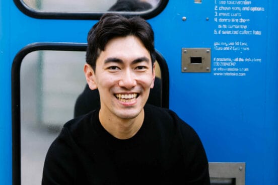 Sung UN Gang sitzt im schwarzen Sweatshirt vor einem blauen Fotoautomaten