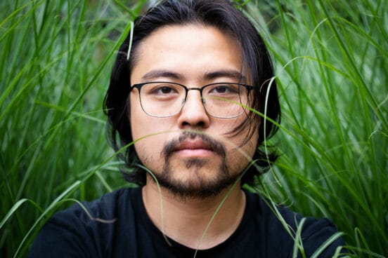Portrait von Theaterregisseur Dan Thy Nguyen im hohen Gras.