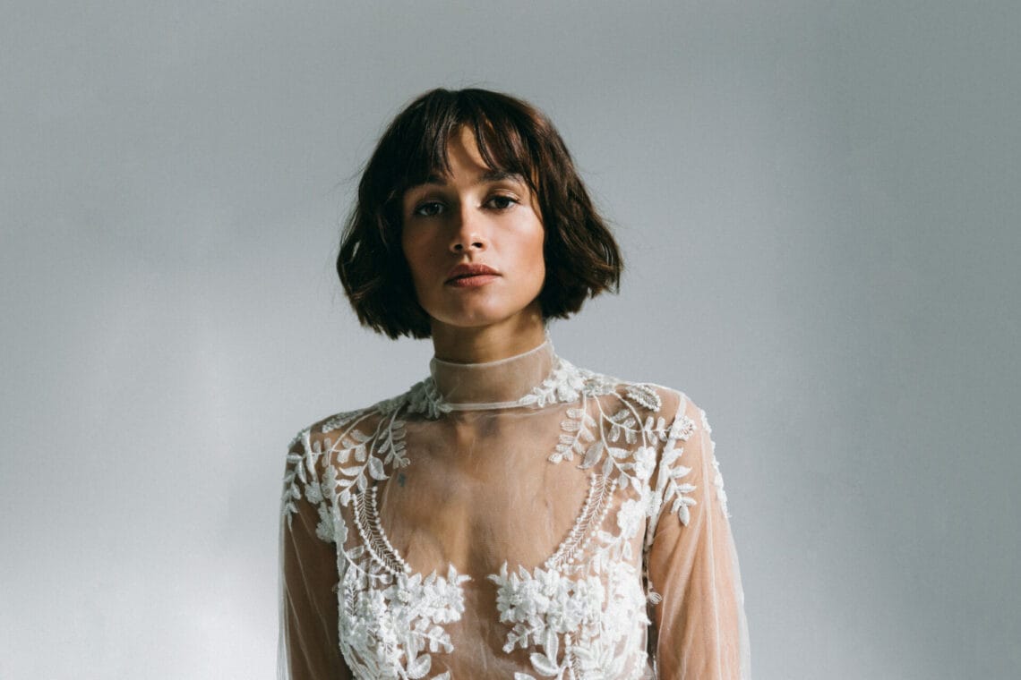 Künstlerin Mogli mit braunem kinnlangem Haar schaut in die Kamera. Sie trägt ein weißes Spitzen-Top.