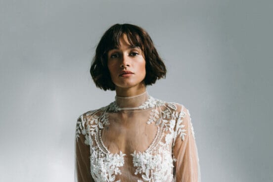 Künstlerin Mogli mit braunem kinnlangem Haar schaut in die Kamera. Sie trägt ein weißes Spitzen-Top.