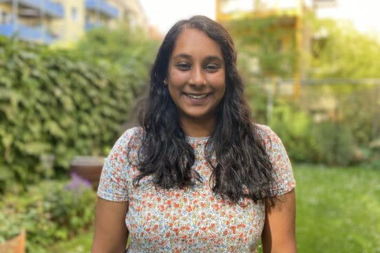 Taudy Padmanathan steht im bunt gepunkteten Oberteil im Garten und lächelt in die Kamera