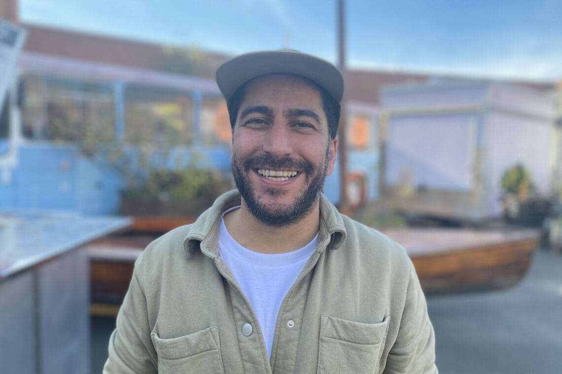 Comiczeichner Hamed Eshrat lächelt in die Kamera. Er trägt ein Käppie und ein beige Cordjacke.