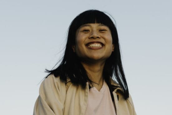 Sängerin Another Nguyen trägt ein hellrosa Short und eine beige dünne Jacke darüber. Sie lächelt von oben in die Kamera